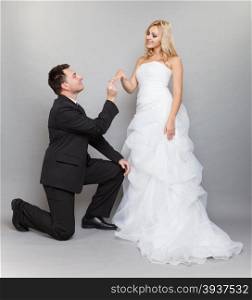 Wedding day. Groom putting a wedding ring on bride&#39;s finger studio shot gray background