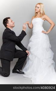 Wedding day. Groom putting a wedding ring on bride&#39;s finger studio shot gray background