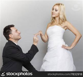 Wedding day. Groom putting a wedding ring on bride&#39;s finger studio shot gray background