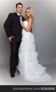 Wedding day. Portrait of happy married couple blonde bride and groom in full length studio shot on gray background