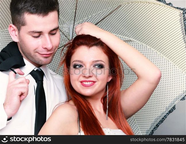 Wedding day. Portrait of happy married couple red haired blue eyed bride and groom with umbrella studio shot on gray background