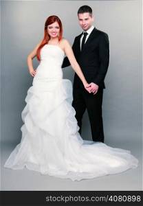 Wedding day. Portrait of happy married couple red haired bride and groom in full length studio shot on gray background