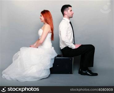 Wedding day. Portrait of happy married couple red haired bride and groom in full length sitting on old suitcase back on back studio shot on gray background. Honeymoon and travel