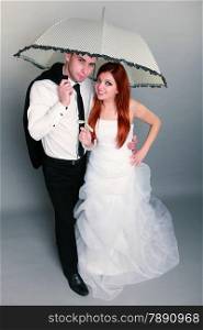Wedding day. Portrait of happy married couple red haired bride and groom in full length with umbrella studio shot on gray background