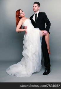 Wedding day. Portrait of happy married couple red haired sexy bride and groom in full length studio shot on gray background
