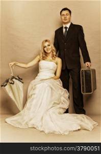 Wedding day. Portrait of married retro couple blonde bride with umbrella and groom with suitcase. Full length studio shot sepia color, vintage photo
