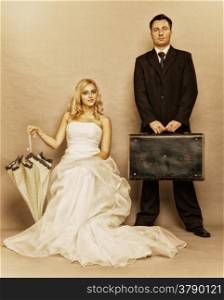 Wedding day. Portrait of married retro couple blonde bride with umbrella and groom with suitcase. Full length studio shot sepia color, vintage photo