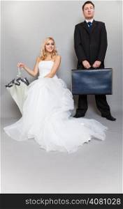 Wedding day. Portrait of married retro couple blonde bride with umbrella and groom with suitcase. Full length studio shot gray background