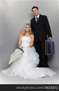 Wedding day. Portrait of married retro couple blonde bride with umbrella and groom with suitcase. Full length studio shot gray background