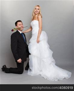 Wedding day. Portrait of romantic married couple blonde bride and enamored groom giving a rose to girl. Full length studio shot gray background