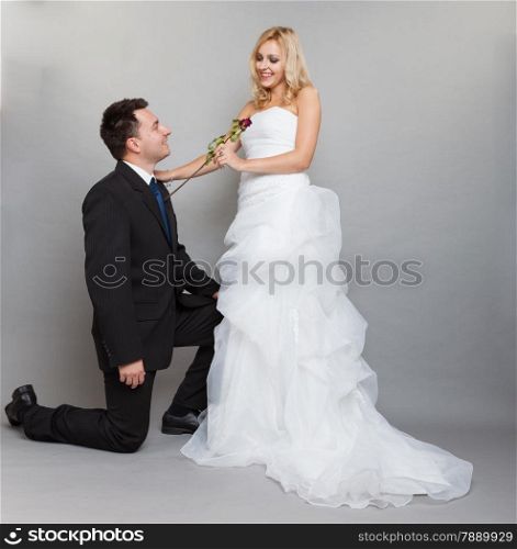 Wedding day. Portrait of romantic married couple blonde bride and enamored groom giving a rose to girl. Full length studio shot gray background