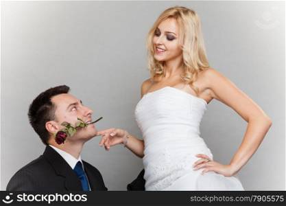 Wedding day. Portrait of romantic married couple blonde bride and enamored groom giving a rose to girl. Studio shot gray background