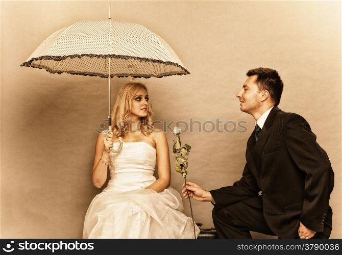 Wedding day. Portrait of romantic married couple blonde bride with umbrella and enamored groom giving a rose to girl. Studio shot sepia color, vintage photo