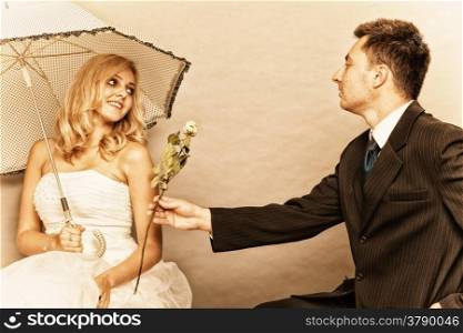 Wedding day. Portrait of romantic married couple blonde bride with umbrella and enamored groom giving a rose to girl. Studio shot sepia color, vintage photo