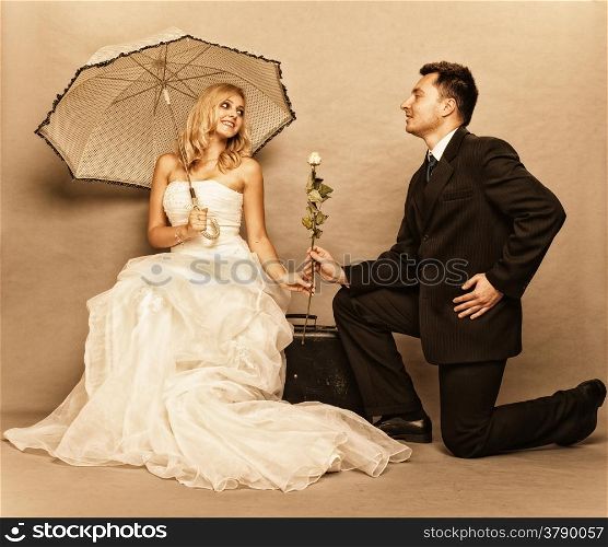 Wedding day. Portrait of romantic married couple blonde bride with umbrella and enamored groom giving a rose to girl. Full length studio shot sepia color, vintage photo