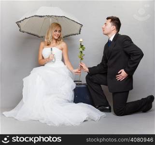 Wedding day. Portrait of romantic married couple blonde bride with umbrella and enamored groom giving a rose to girl. Full length studio shot gray background
