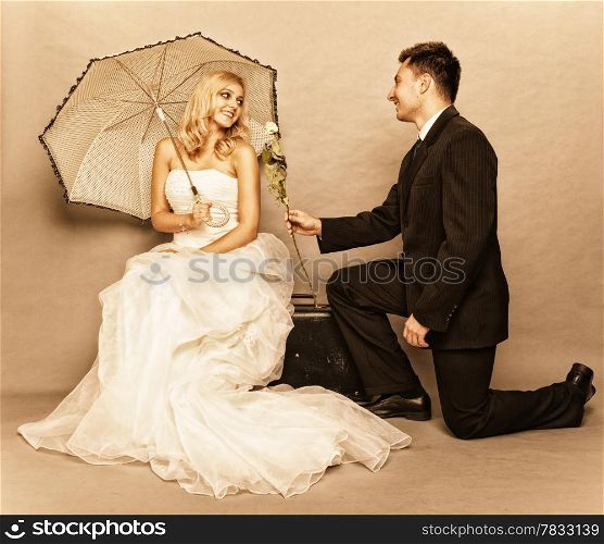 Wedding day. Portrait of romantic married couple blonde bride with umbrella and enamored groom giving a rose to girl. Full length studio shot sepia color, vintage photo