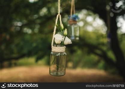 Wedding decorations from small bottles filled with roses and other flowers suspended on a thread between trees in the woods