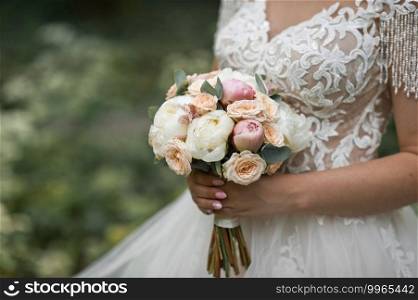 Wedding delicate bouquet of peonies and buds in the hands of the bride.. Round wedding bouquet of delicate pink and white peonies 2565.