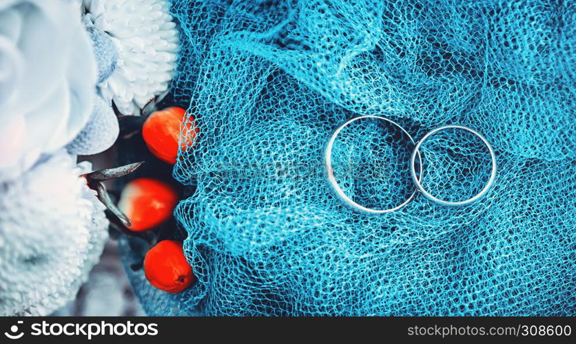 Wedding engagement rings on blurred blue background with white and red flowers. Shallow soft selective focus.. Wedding Engagement Rings