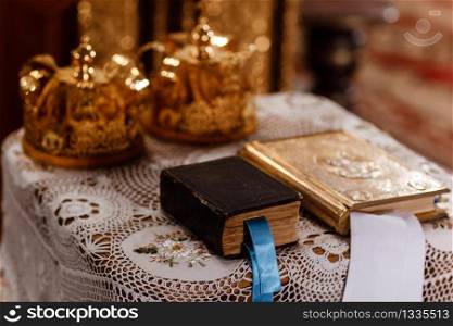 wedding Golden crowns and bible on the table in church. Wedding crowns in church ready for marriage ceremony. close up. Divine Liturgy. selective focus.. wedding Golden crowns and bible on the table in church. Wedding crowns in church ready for marriage ceremony. close up. Divine Liturgy. selective focus