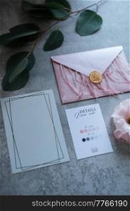 wedding invitation in a gray envelope on a table with green sprigs