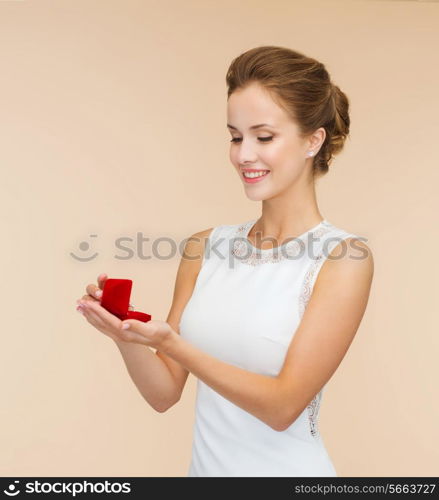 wedding, love, engagement and happiness concept - smiling woman in white dress holding red gift box with diamond ring over beige background