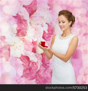wedding, love, engagement and people concept - smiling woman in white dress holding red gift box with diamond ring over pink floral background