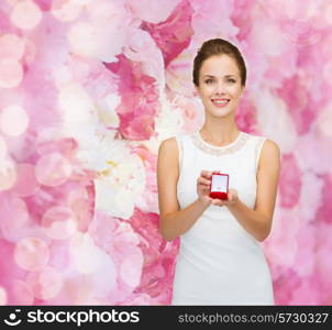 wedding, love, engagement and people concept - smiling woman in white dress holding red gift box with diamond ring over pink floral background