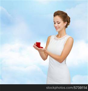 wedding, love, engagement and people concept - smiling woman in white dress holding red gift box with diamond ring over blue cloudy sky background