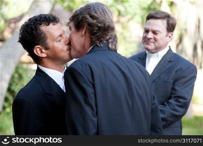 Wedding of handsome gay male couple. The grooms kiss as the minister looks on.