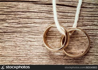 Wedding rings hanging on rope over wooden background. Vintage image.