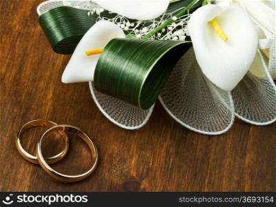 Wedding rings with calla bouquet on wooden background