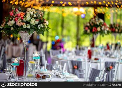 Wedding table decoration. Beautiful bouquet of flowers in vase on the table, next to plates, glasses and gift boxes. Bouquet of flowers, glasses, gift boxes and jugs setting on the festive table in restaurant.
