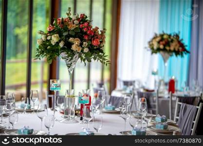 Wedding table decoration. Beautiful bouquet of flowers on the table, next to plates,  glasses and gift boxes. Bouquet of roses and glasses on the wedding table.