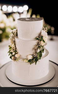 wedding white cake on a high stand near the white podium with green decor