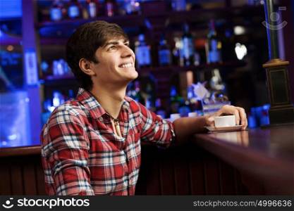 Weekend evening. Young handsome man in casual sitting at bar