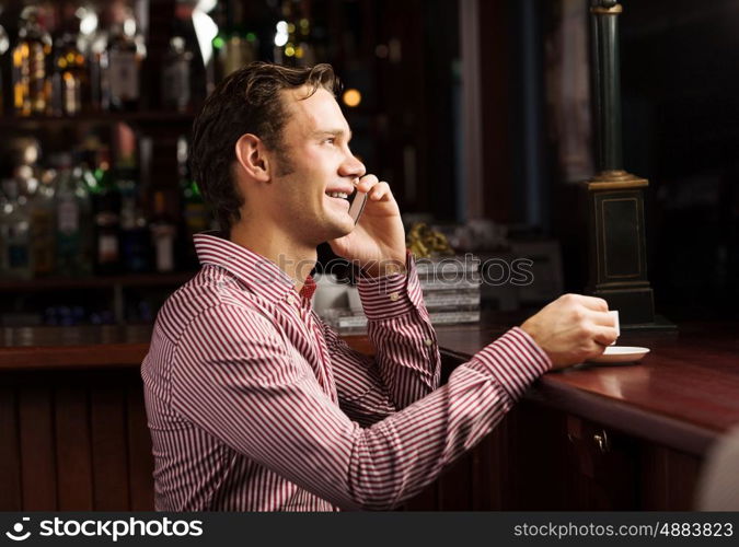 Weekend evening. Young handsome man in casual sitting at bar and talking on phone