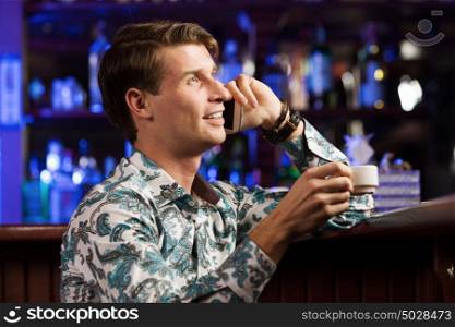 Weekend evening. Young handsome man in casual sitting at bar and talking on phone