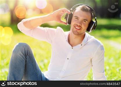 Weekend in park. Handsome male in park wearing headphones and listening music