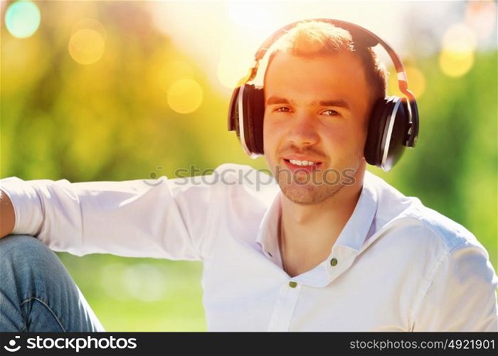 Weekend in park. Handsome male in park wearing headphones and listening music