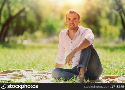 Weekend in park. Handsome man sitting on the green grass in park