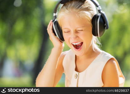 Weekend in park. Little cute girl in summer park on blanket wearing headphones