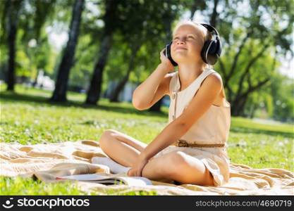 Weekend in park. Little cute girl in summer park on blanket wearing headphones