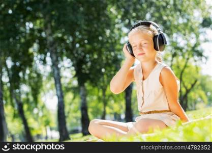 Weekend in park. Little cute girl in summer park on blanket wearing headphones