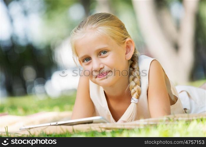 Weekend in park. Little cute girl in summer park on blanket with tablet pc