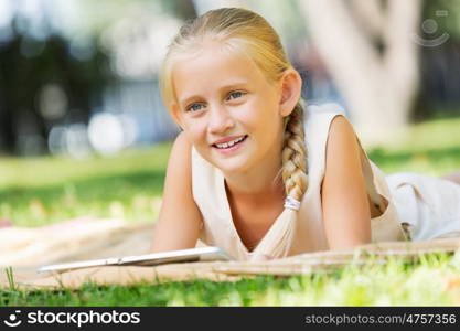 Weekend in park. Little cute girl in summer park on blanket with tablet pc