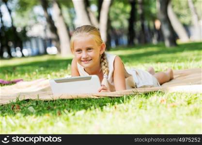 Weekend in park. Little cute girl in summer park on blanket with tablet pc
