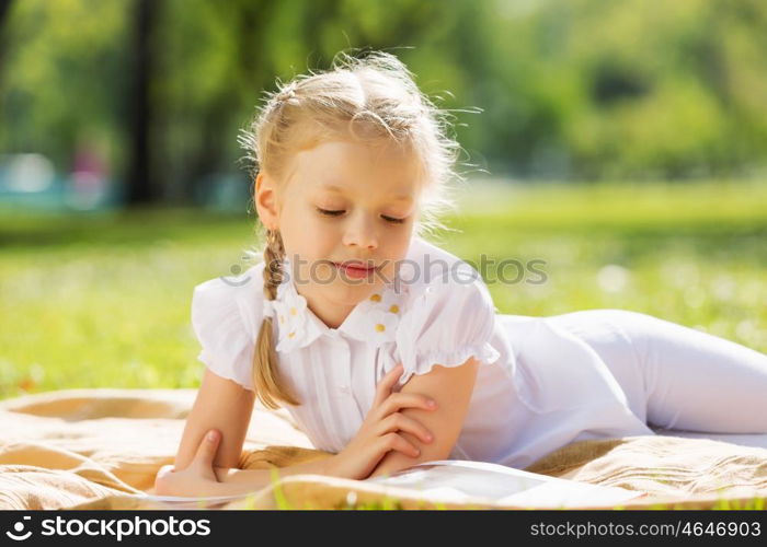 Weekend in park. Little cute girl in summer park reading book