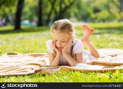 Weekend in park. Little cute girl in summer park reading book